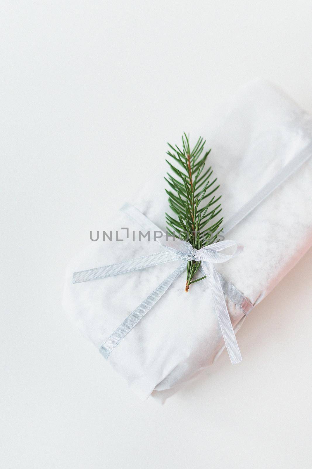 A homemade Christmas stollen sealed in white craft paper, along with a sprig of a Christmas tree, lies on a white background. Gift wrap