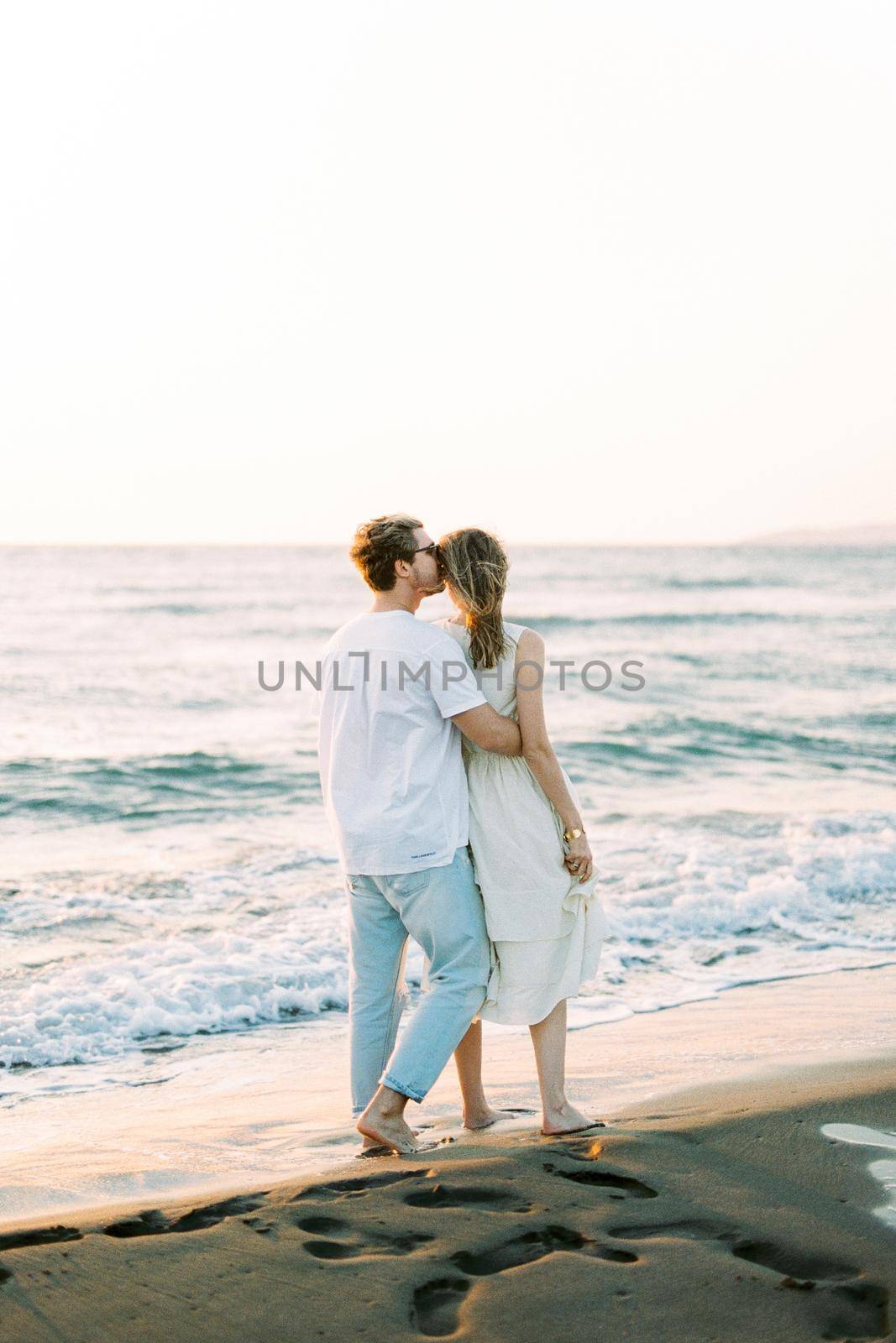 Man hugs and kisses woman on the temple while standing on the beach. Back view. High quality photo