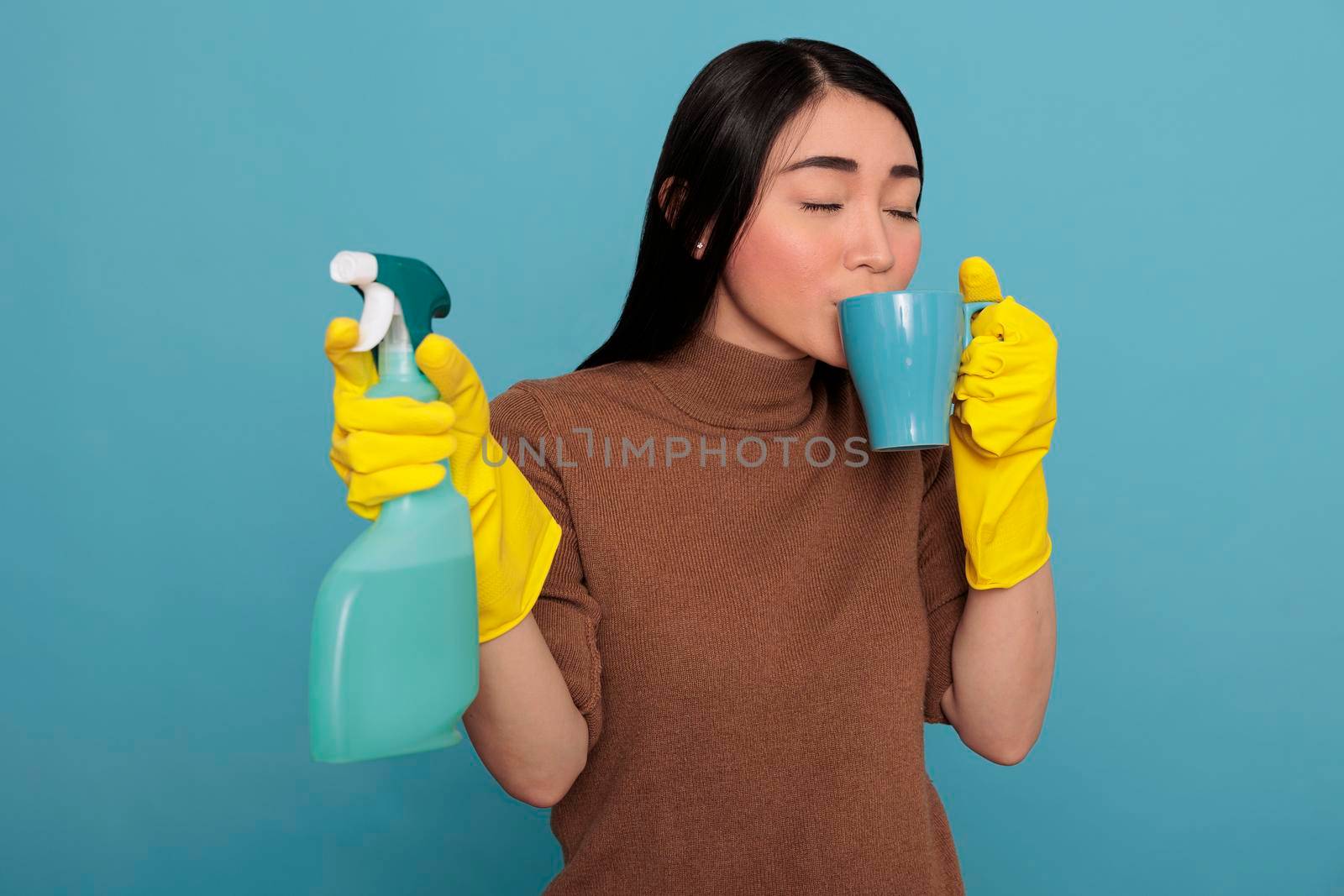 Tired exhausted young asian housewife taking coffee during work break while holding a sponge in the other hand, Cleaning home concept, Refreshment tea take some rest from day to day chores,