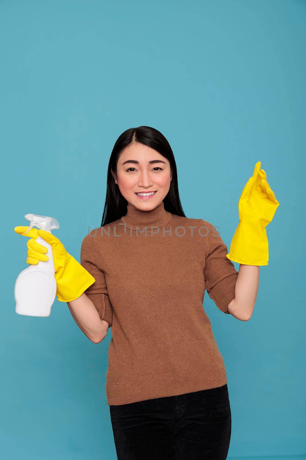 Satisfied smiling asian housemaid holding spray yellow rubber glove isolated on a blue background, Cleaning home concept, Smiling face expression female ready to do household duties