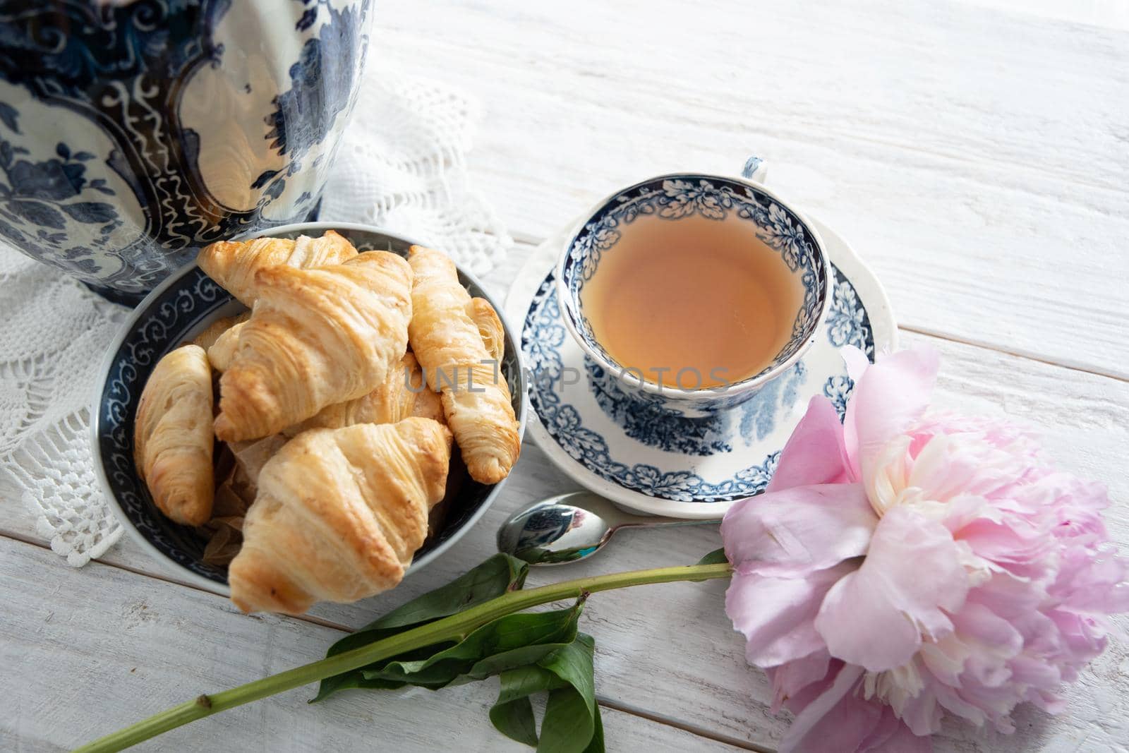 spring still life with croissants and a bouquet of pink luxurious peonies in an ancient Chinese vase with blue ornament, an antique tea cup, early breakfast or brunch, High quality photo