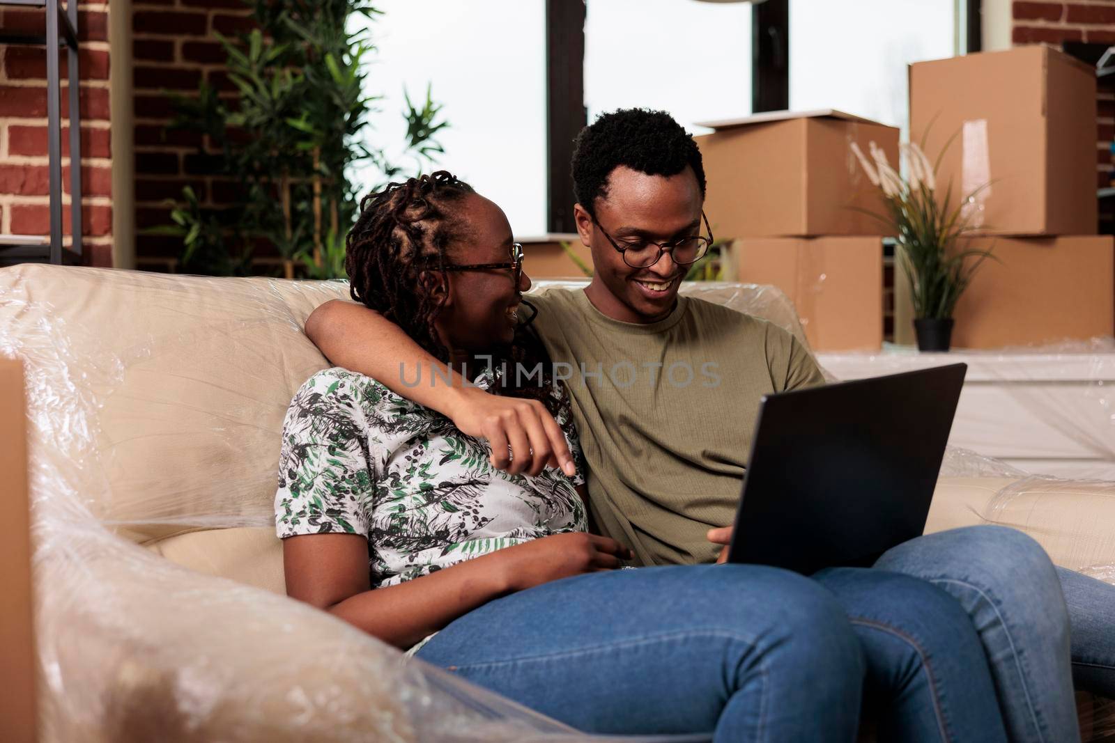 Happy married couple finding furniture on online website, shopping on laptop to decorate rented flat. Buying decorations on internet browser after moving in new household property.