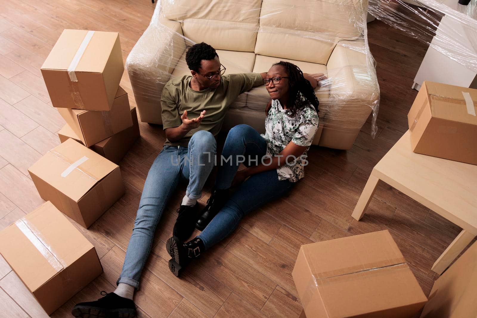 African american people sitting on apartment floor after moving in and relocating in new property. Feeling relaxed and happy about starting new beginnings, celebrating life event. Top view of.