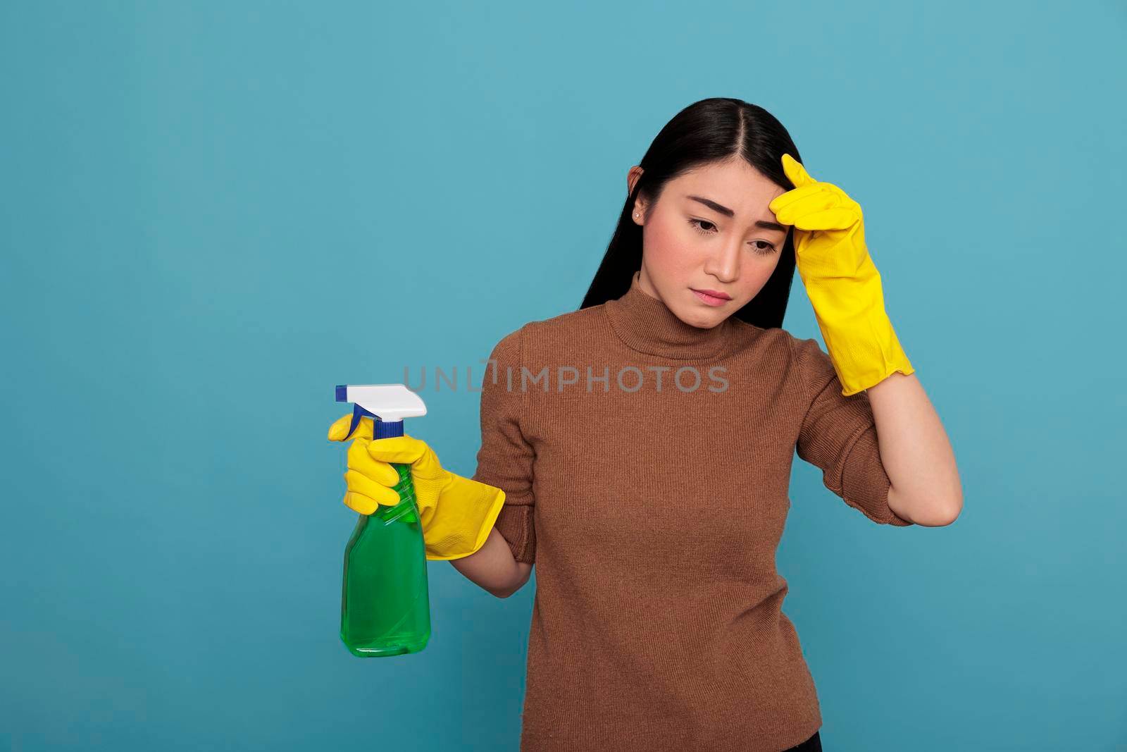 Tired stressed and frustrated asian housewife at work holding spray detergent in yellow rubber glove, Cleaning home concept, Sad unhappy and exhausted housemaid negative from chores