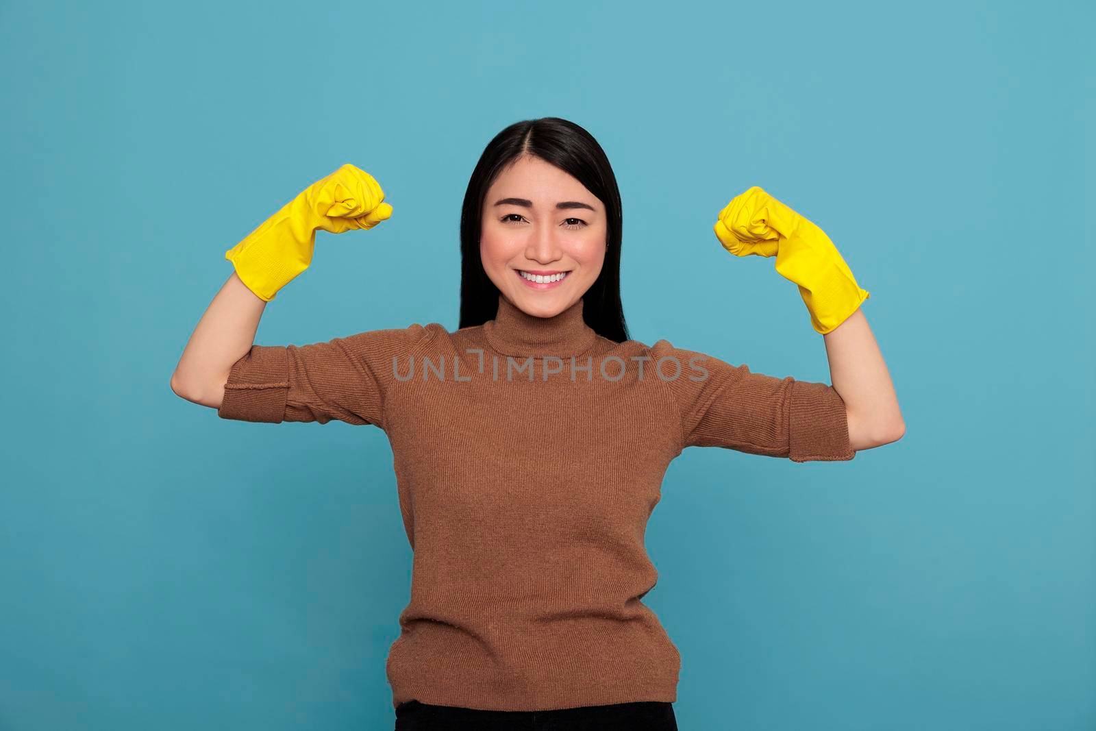 Happy energetic beautiful asian housewife raising arms and showing biceps isolated blue background, Housewife worker, Cleaning home concept, Female smiling after completing his job,