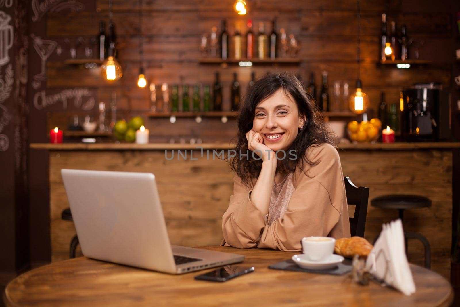 Portrait of smillig young woman in a coffee shop with modern computer near her. Coffee shop with wireless connection on the internt. Cheerul young woman sitting down in a coffee shop.