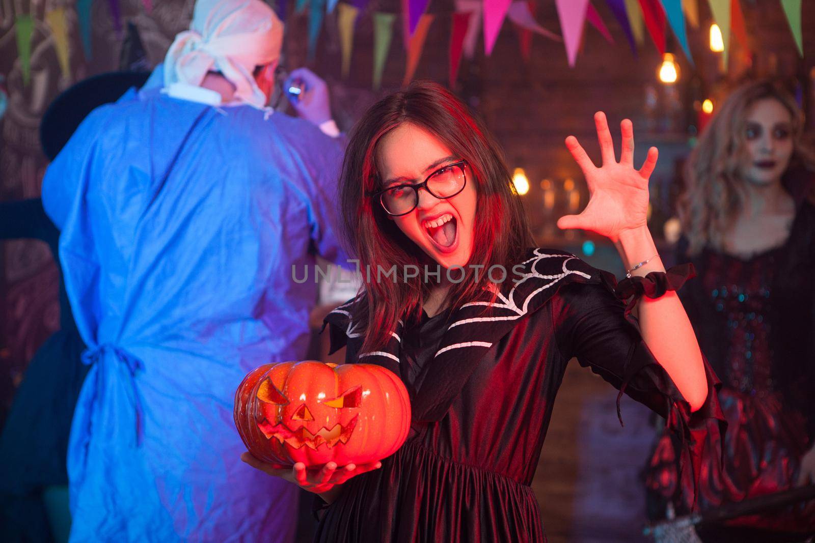 Girl screaming to the camera dressed up like a witch with a pumpking celebrating halloween with her friends.