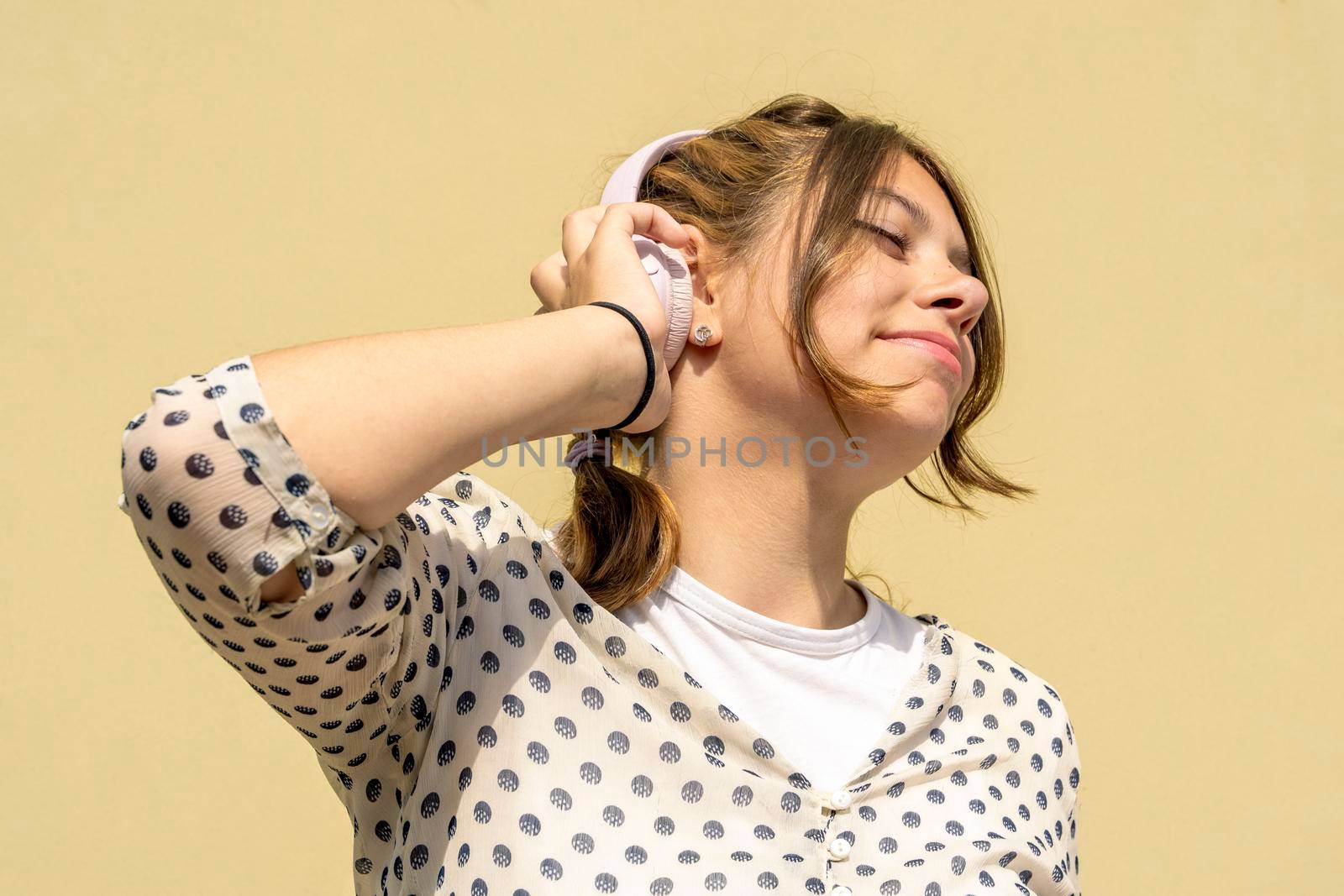 Teenage cute Caucasian girl has a good time listening to music with headphones. a beautiful fashionable girl enjoys music. a girl is dancing, listening to music with headphones, closing her eyes, against a yellow background