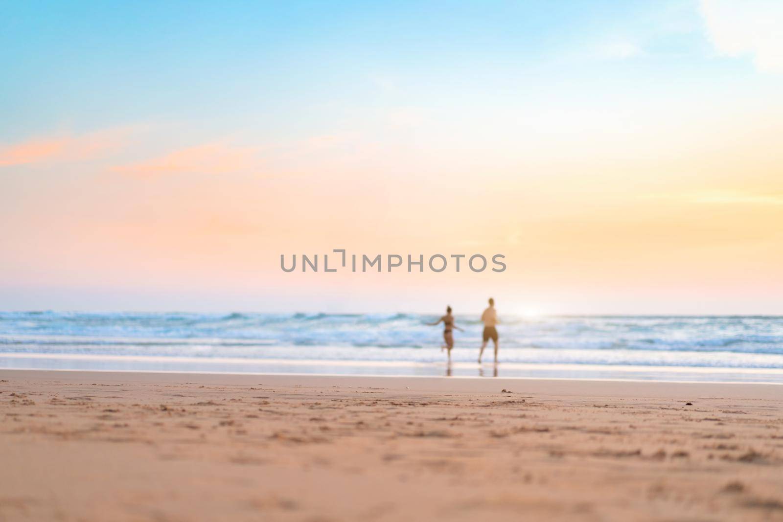 Couple running on the beach. Happy couple go to swim in ocean at sunset. Blurred summer vacation background. Defocused man and woman run on sandy sea beach. Summertime. Happy people