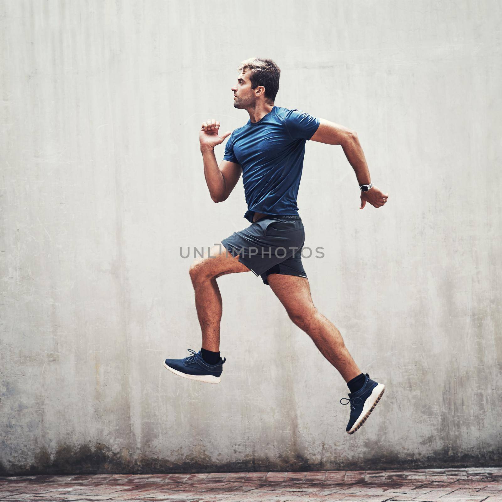 Skip over every hurdle until you reach your goal. a sporty young man running against a grey wall outdoors. by YuriArcurs