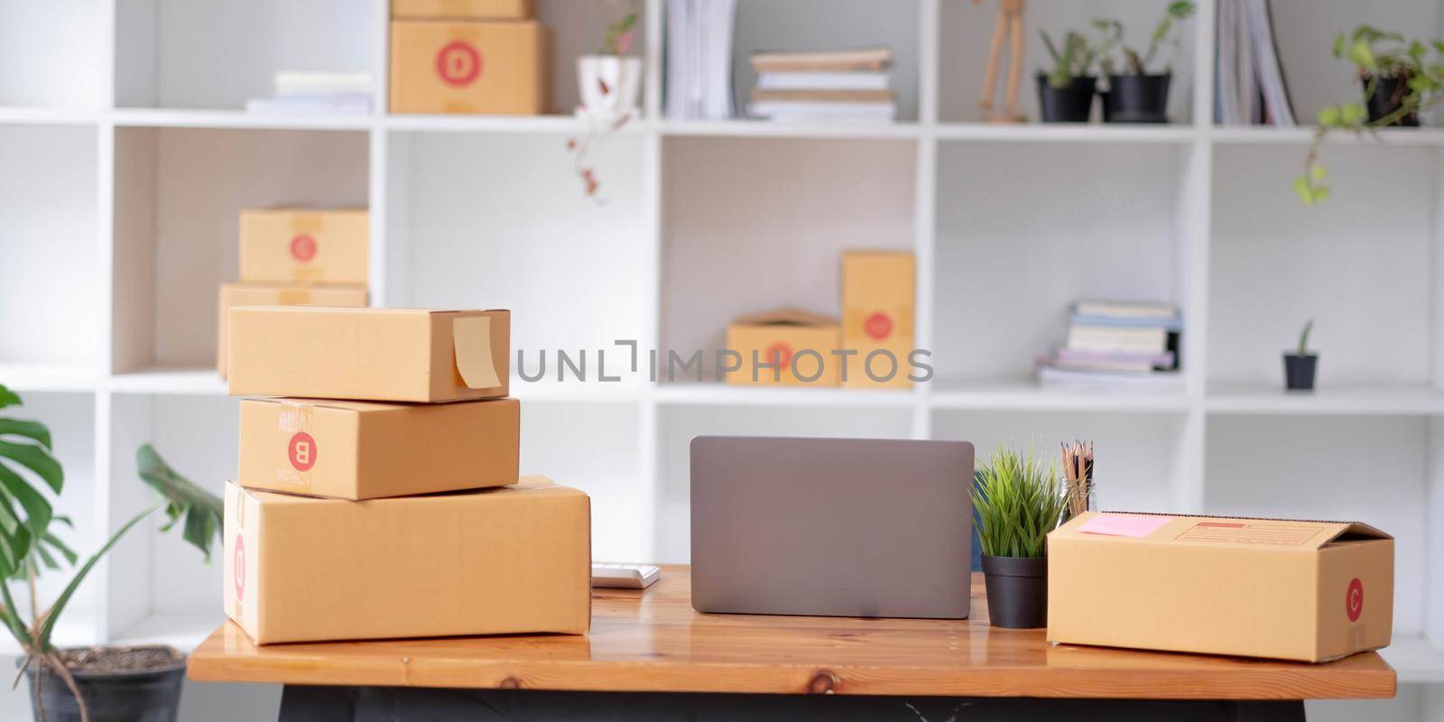 Parcel boxes on shelf and color shopping bags placing near laptop on table. SME business on shopping online at home office packaging on background is popular business..