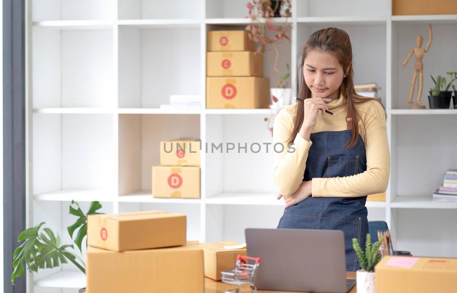 Startup small business entrepreneur or freelance Asian woman using a laptop with box, Young success Asian woman with her hand lift up, online marketing packaging box and delivery, SME concept..