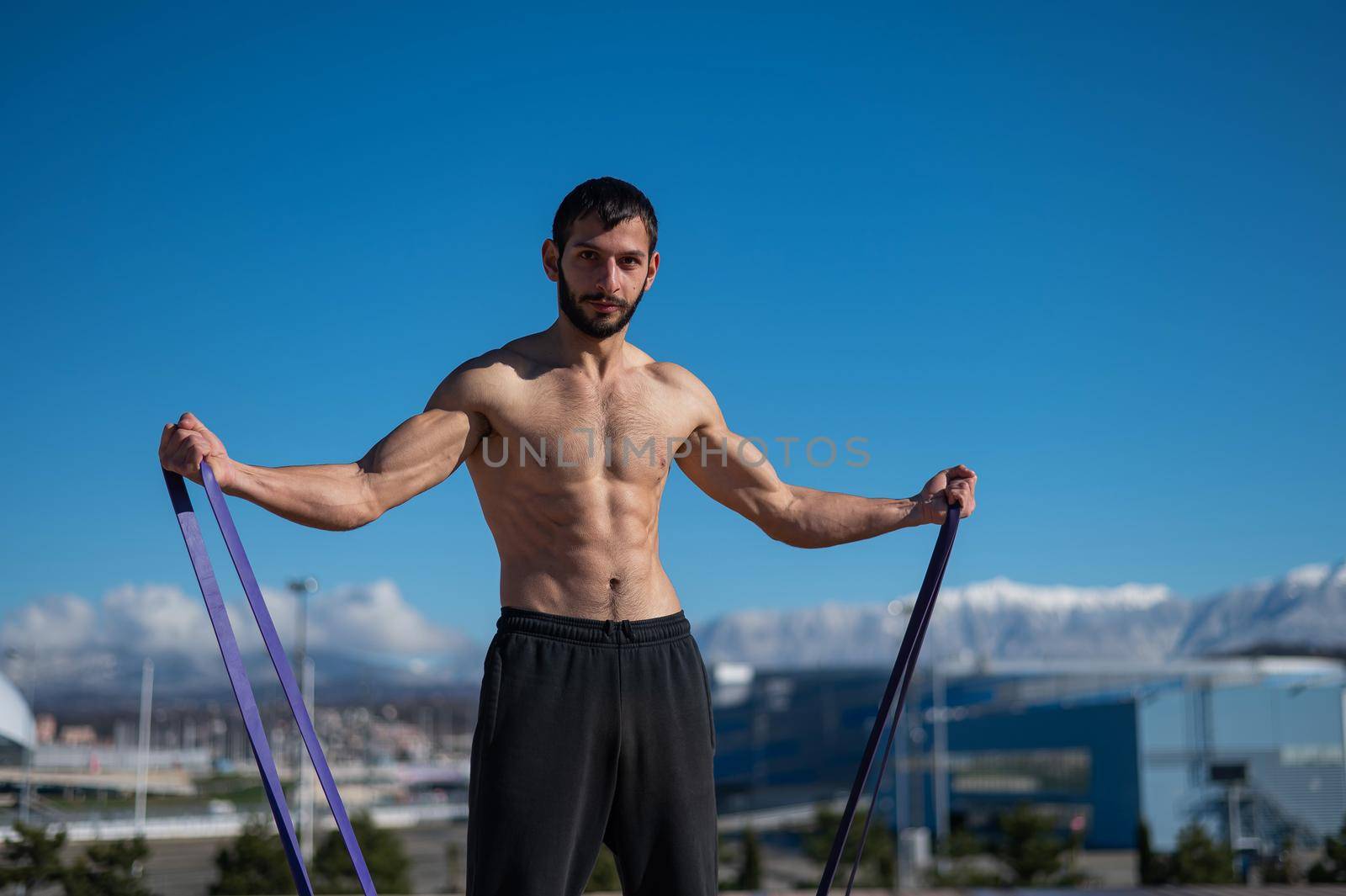 Shirtless man doing exercise with rubber bands outdoors