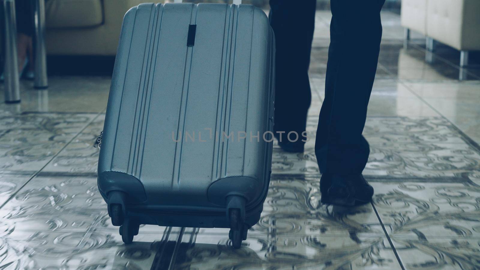 legs of businessman walking through hotel lobby pulling luggage and stop at reception desk. Business, travel and people concept by silverkblack