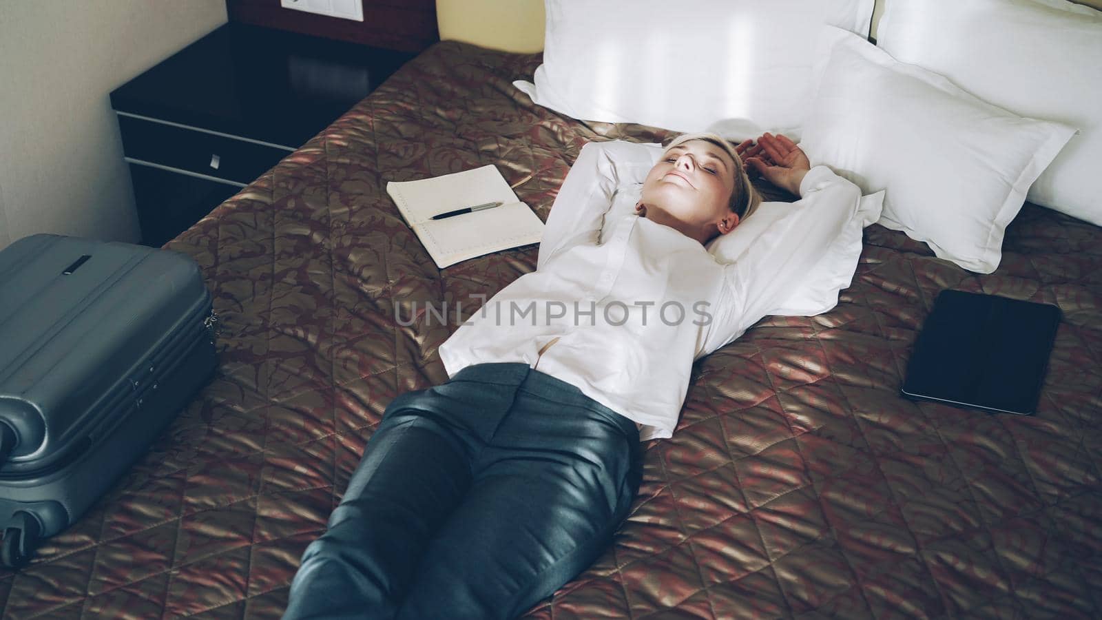 Smiling businesswoman lying on bed relaxed in hotel room. Travel, business and people concept by silverkblack