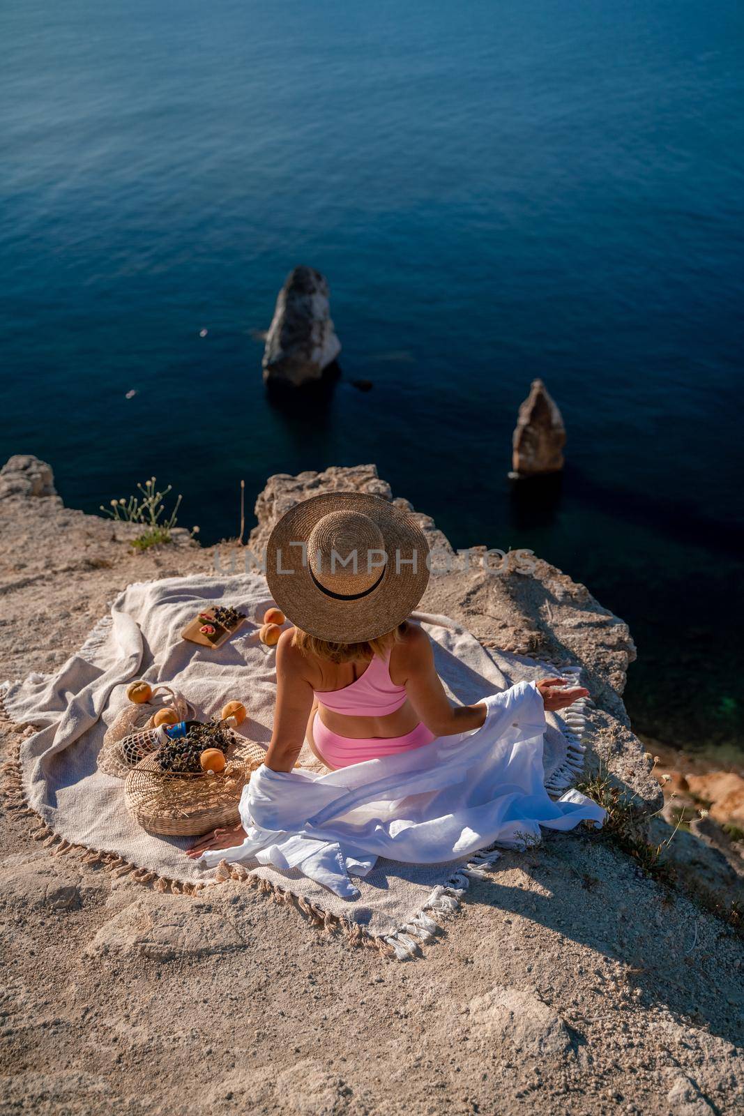 photo of a beautiful woman with long blond hair in a pink shirt and denim shorts and a hat having a picnic on a hill overlooking the sea by Matiunina