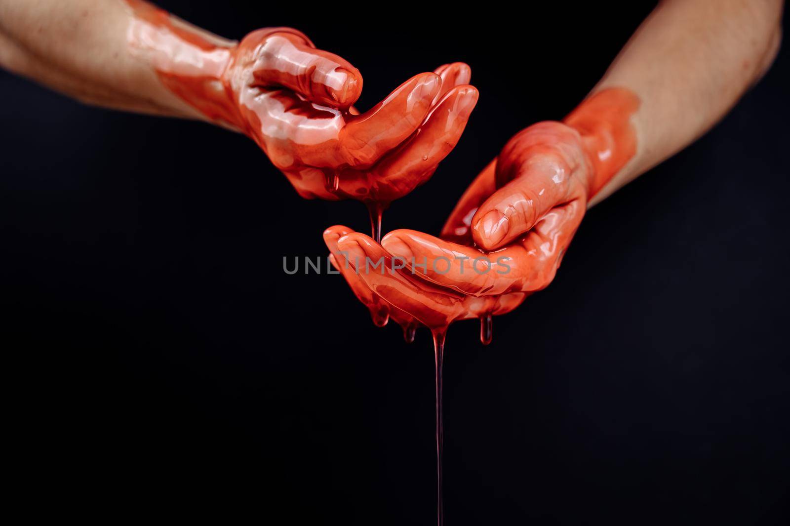 Women's hands in a viscous red liquid similar to blood