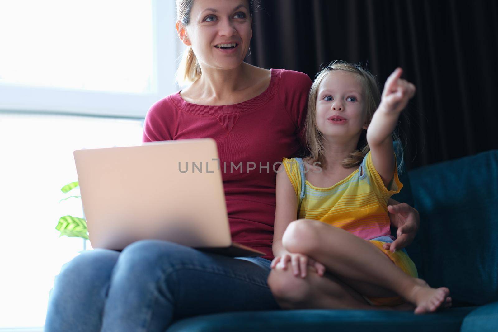 Portrait of mother and child sitting on sofa with laptop looking away in surprise. Emotions of surprise and delight