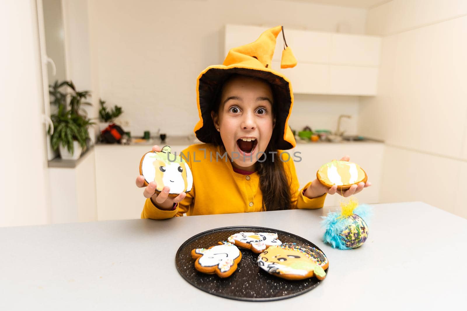 Little girl in Halloween costume plays with gingerbread cookies like a pumpkin.