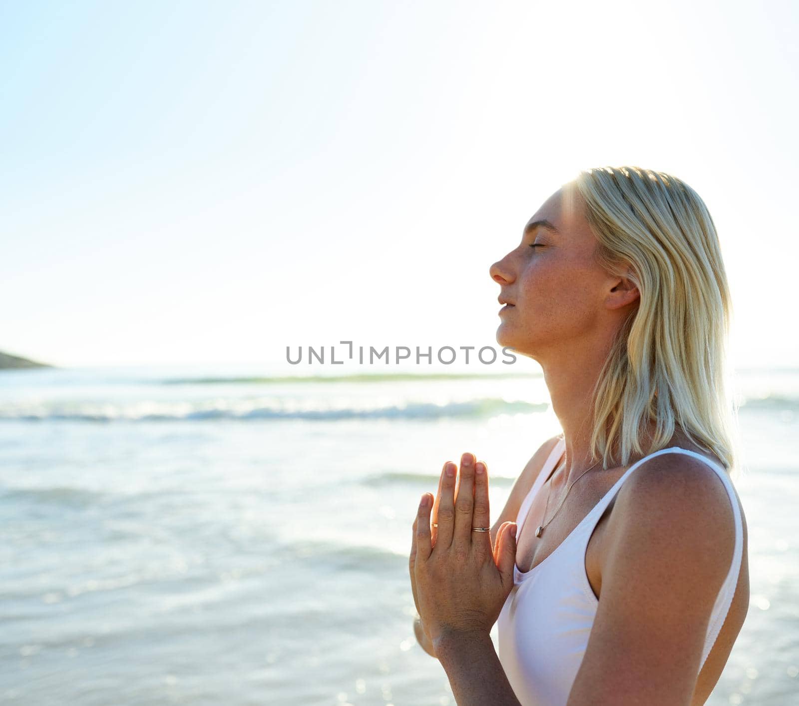 Finding the peace within my soul. an attractive young woman meditating early in the morning on the beach. by YuriArcurs