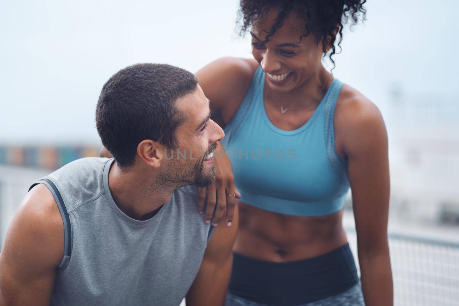 This healthy lifestyle really suits us well. a sporty young couple taking a break while exercising outdoors. by YuriArcurs