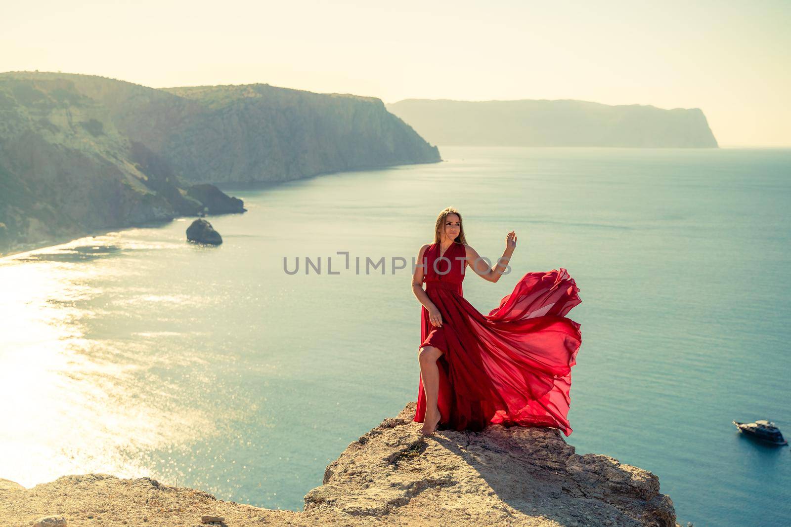 A woman in a red flying dress fluttering in the wind, against the backdrop of the sea