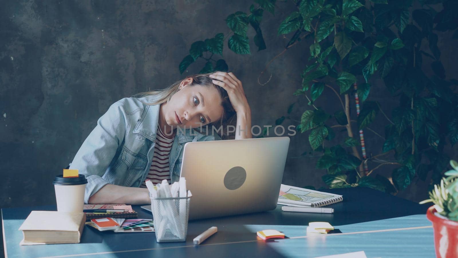 Young blond woman is sitting in office working with computer. She is tired after long day at work by silverkblack