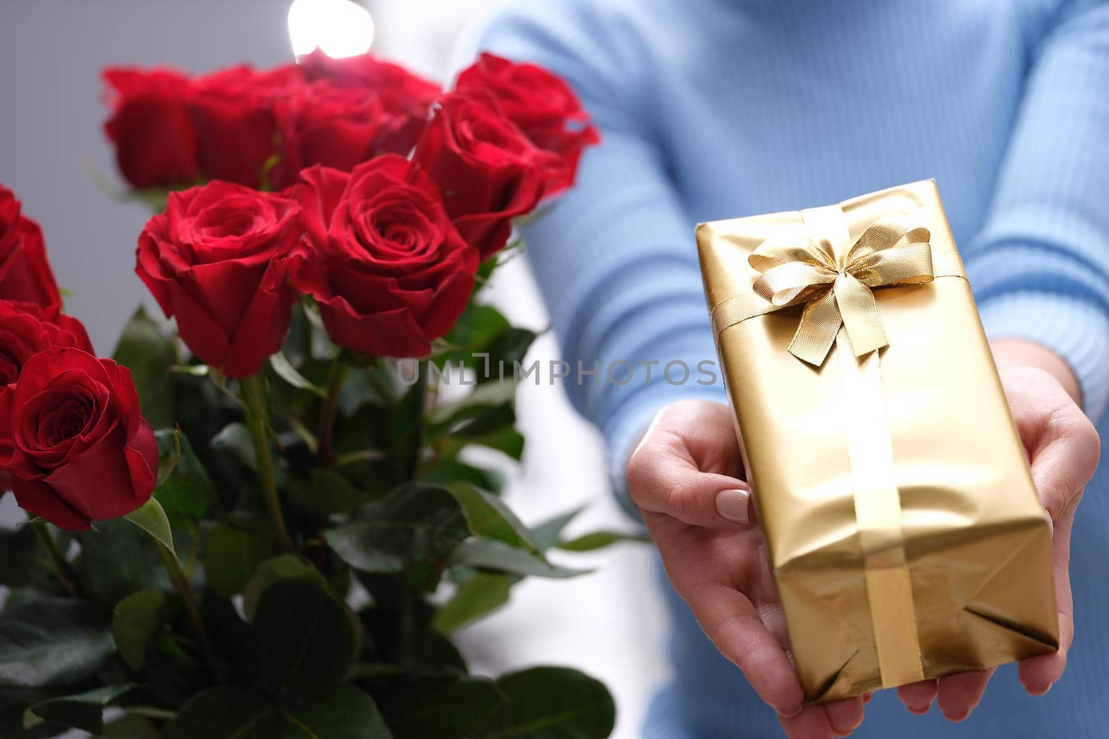 Bouquet of red roses and golden gift box in hands of courier. Delivery of romantic gifts concept