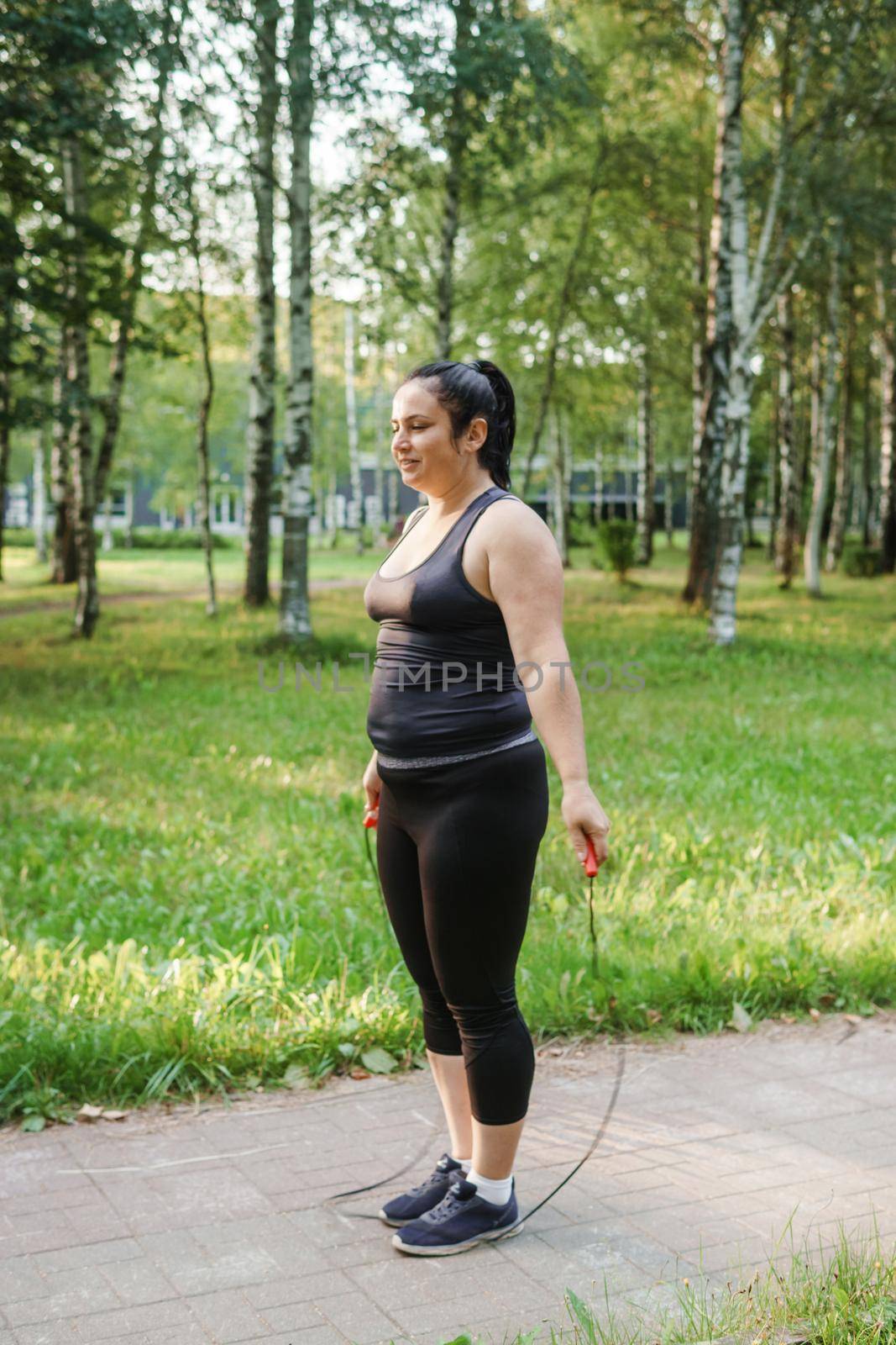 A charming brunette woman plus-size body positive practices sports in nature.