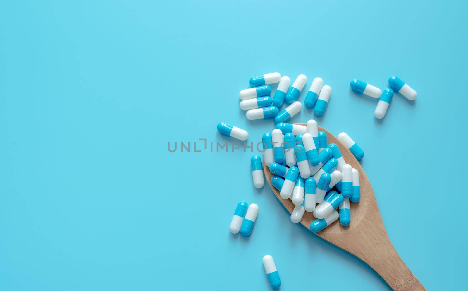 Blue-white capsule pills on wooden spoon. Capsule pills on blue background. Health topics. Drug for treatment illness. Medication use. Medical care. Pharmaceutical industry. Capsule pill production.