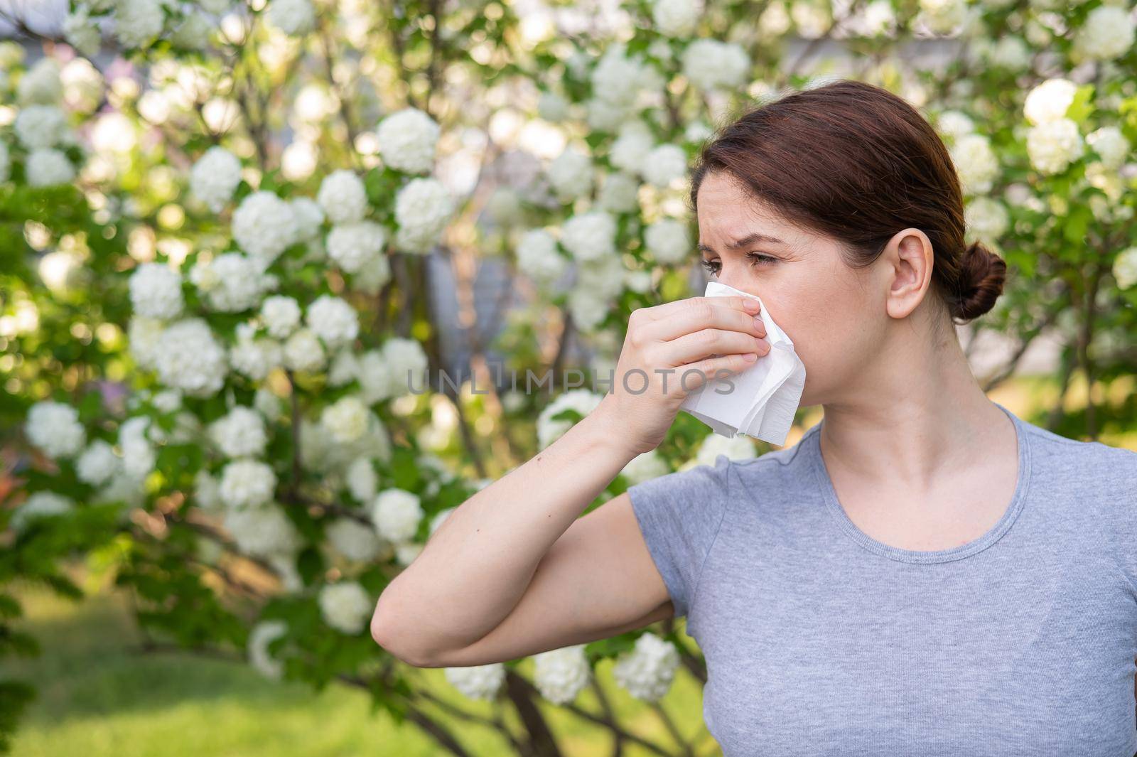 Middle-aged woman blowing her nose in a flowering garden