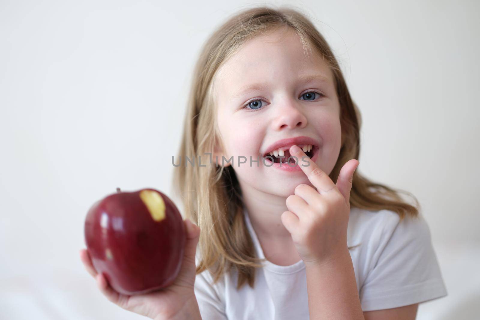 Portrait of smiling cute girl without teeth with red bitten apple in hand by kuprevich