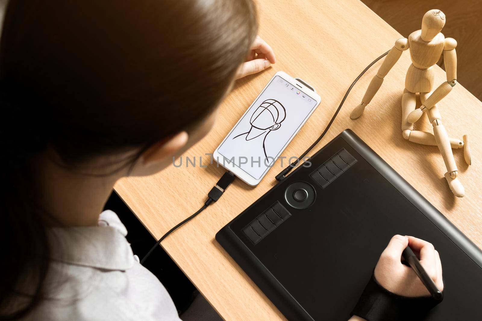 Woman artist sketching of human head on phone with graphic tablet and drawing mannequin, top view, modern technology concept, neutral colors and soft beige earth tones