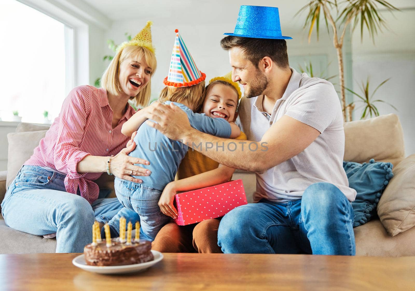 Family of four, mother, father, daughter and son having fun celebrating a birthday together with birthday cake and candles and a present at home