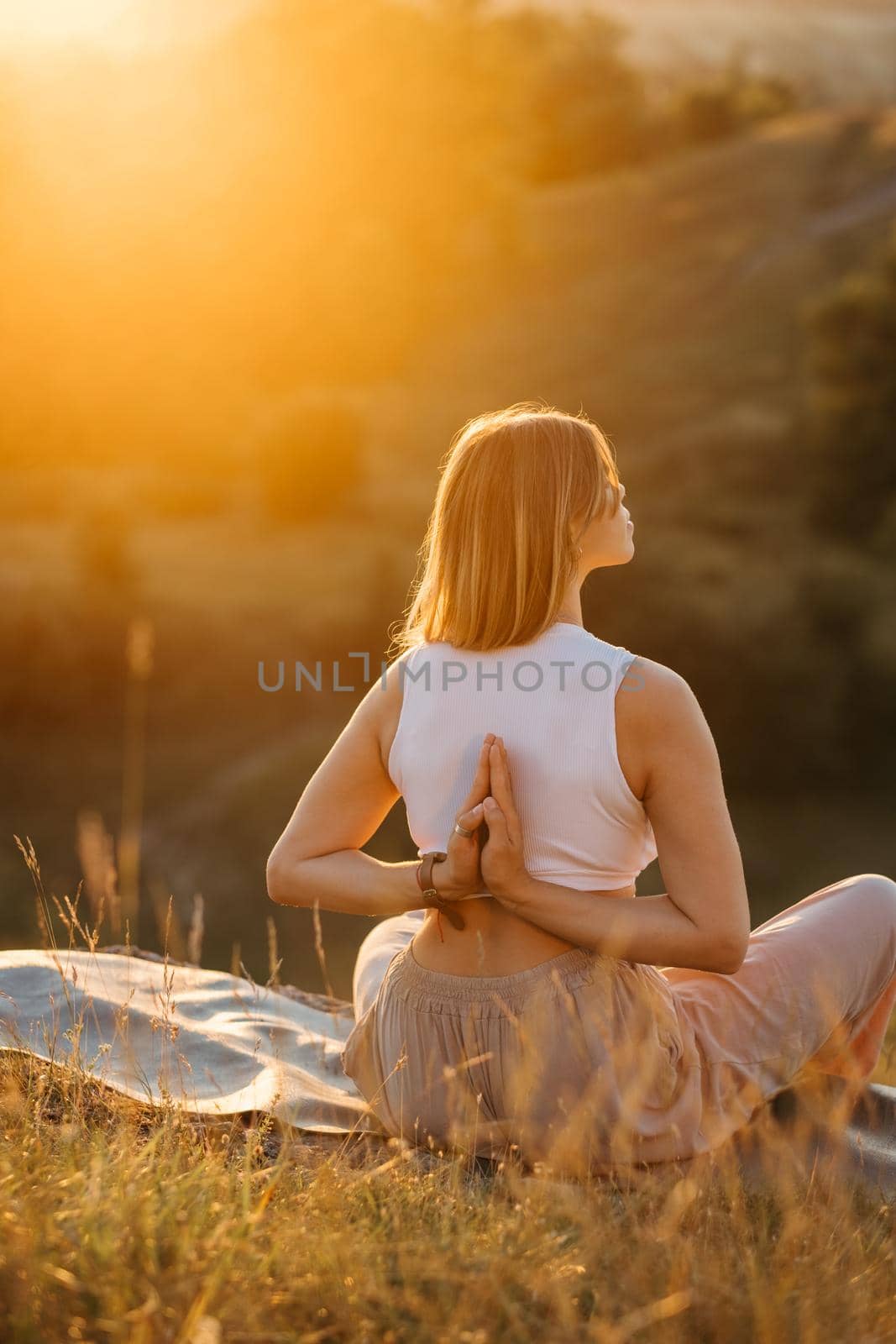 Young Woman with Folded Hands on Back Meditating and Enjoying Beautiful Sunset Outdoors