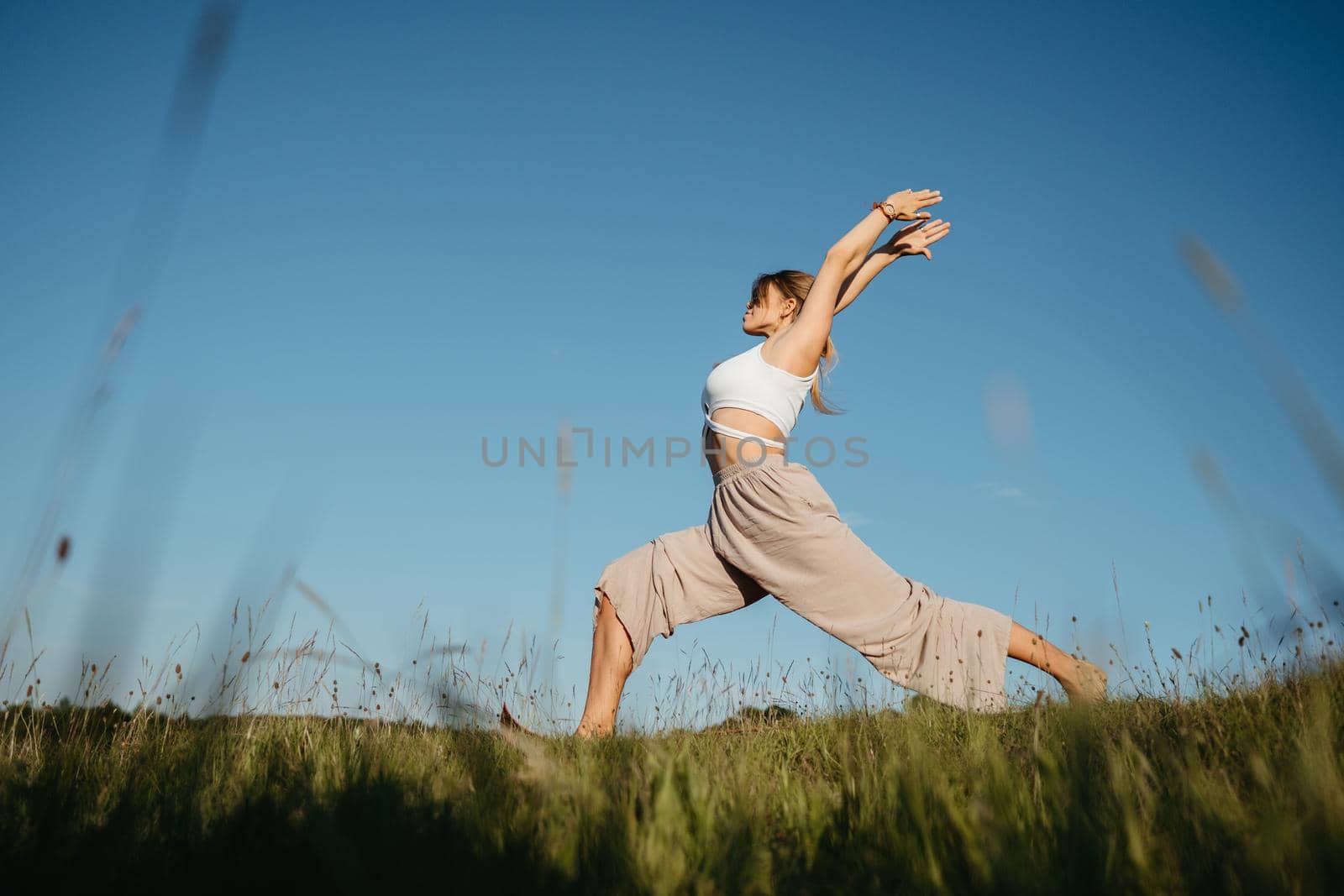 Young Woman Practicing Yoga Outdoors in the Field with Blue Sky on Background
