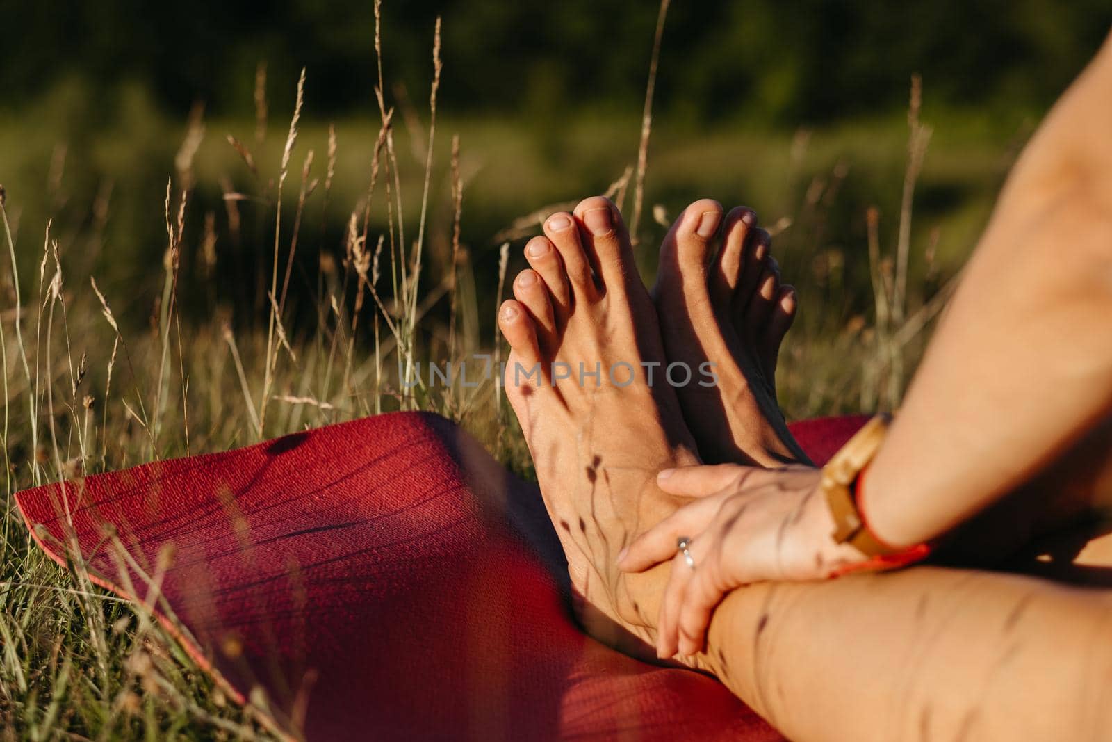 Close Up Unrecognisable Woman Holding Her Feet While Sitting on the Mat During Yoga Outdoors at Sunset by Romvy