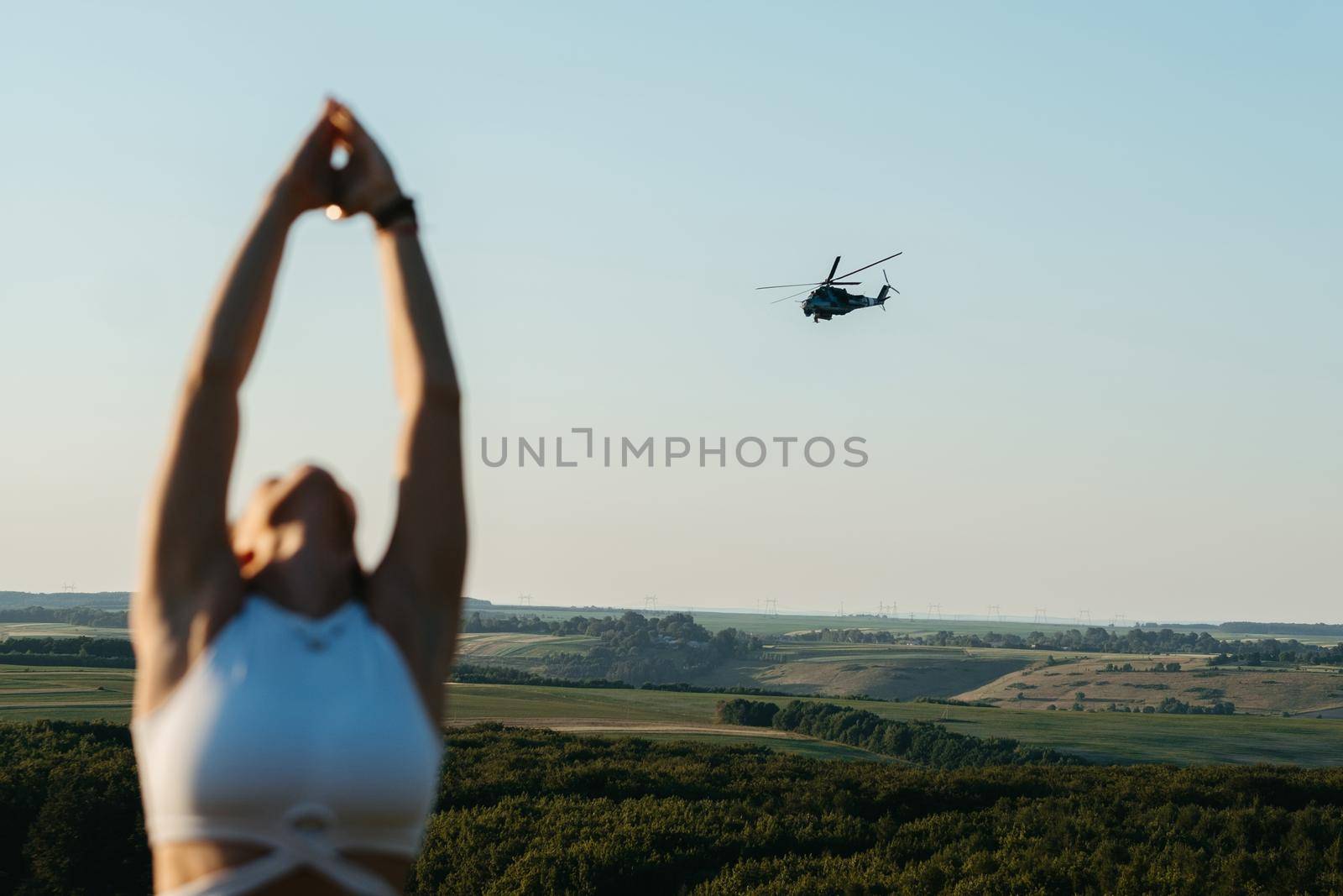 Unrecognisable Woman Meditating and Practicing Yoga Outdoors in Ukraine at Sunset with Scenic Landscape and Combat Helicopter on Background