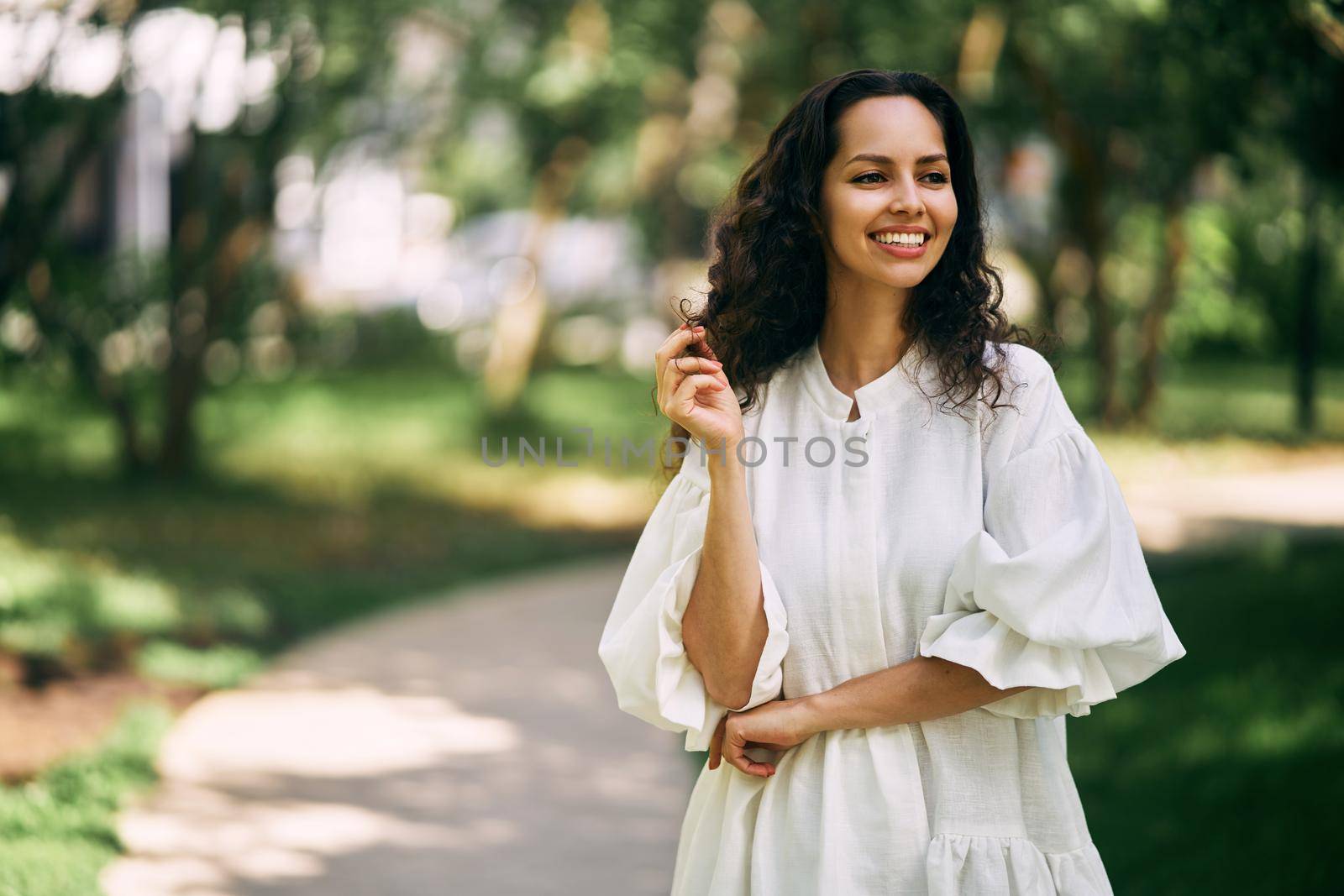 Portrait of a beautiful curly-haired brunette girl in the park. Girl smiling and holding her hair by driver-s