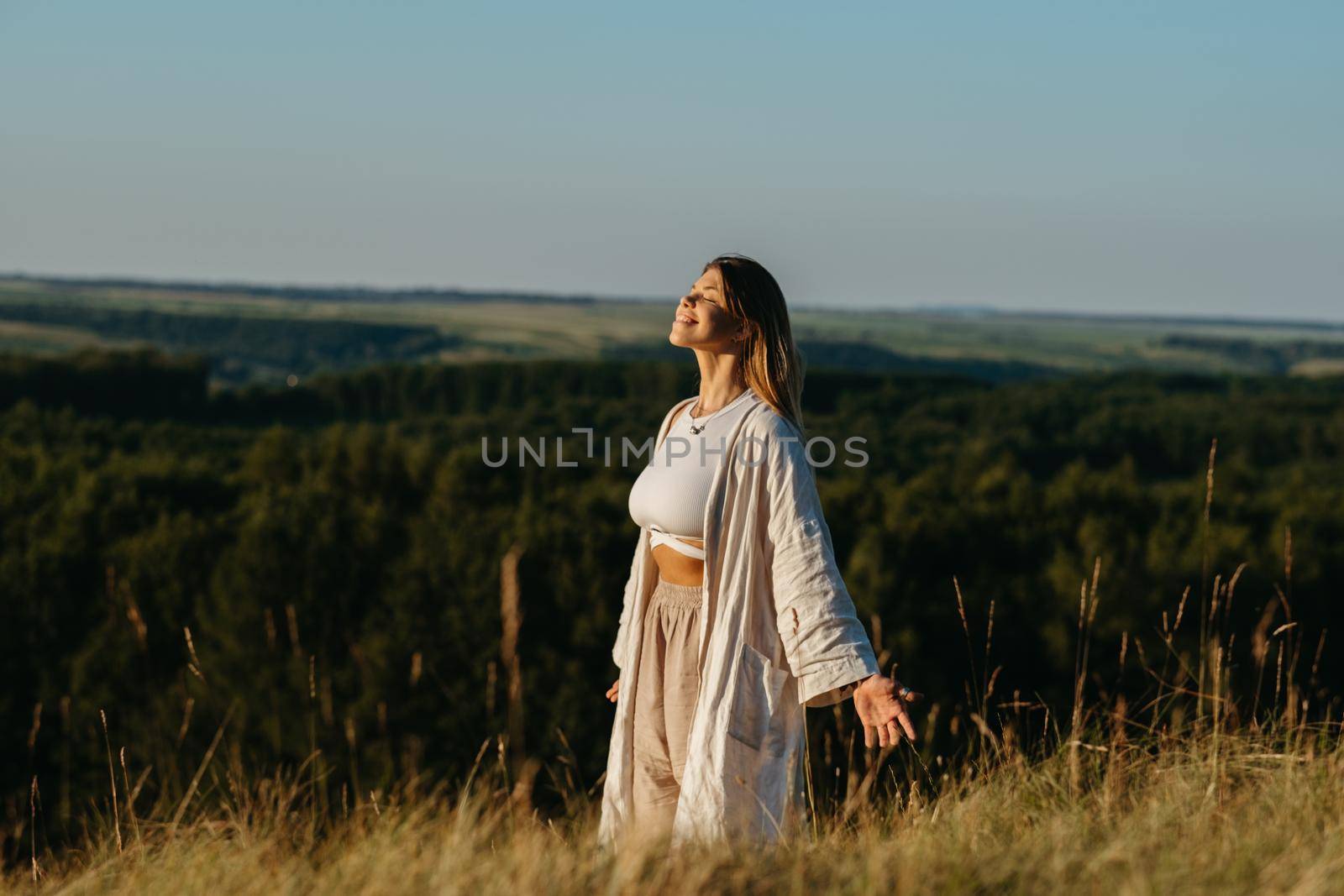 Happy Young Woman Meditating and Catching Sunlight Outdoors at Sunset with Scenic Landscape on Background