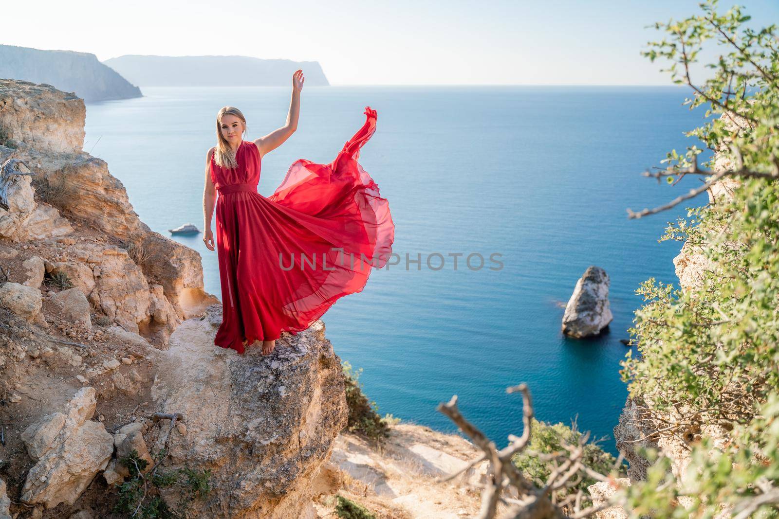 A woman in a red flying dress fluttering in the wind, against the backdrop of the sea. by Matiunina