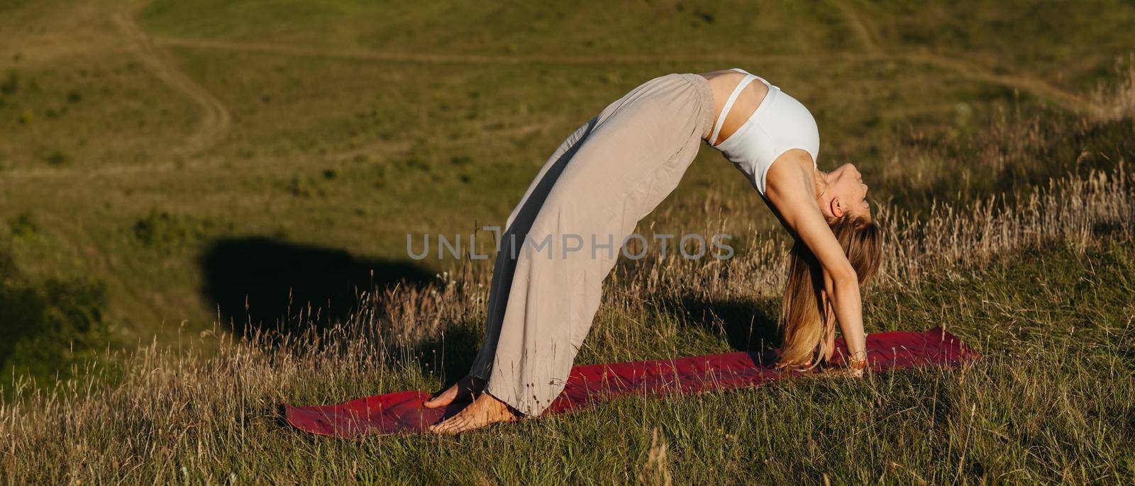 Young Woman Doing Bridge Exercise During Yoga Practice Outdoors with Beautiful Background by Romvy