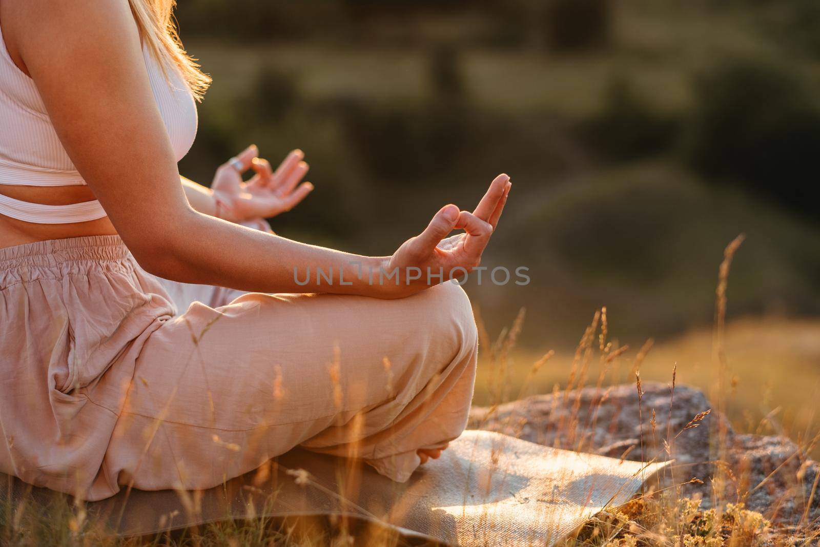 Unrecognisable Woman Connecting Fingers on Hands While Sitting on Mat, Concept of Meditation Outdoors at Sunset by Romvy