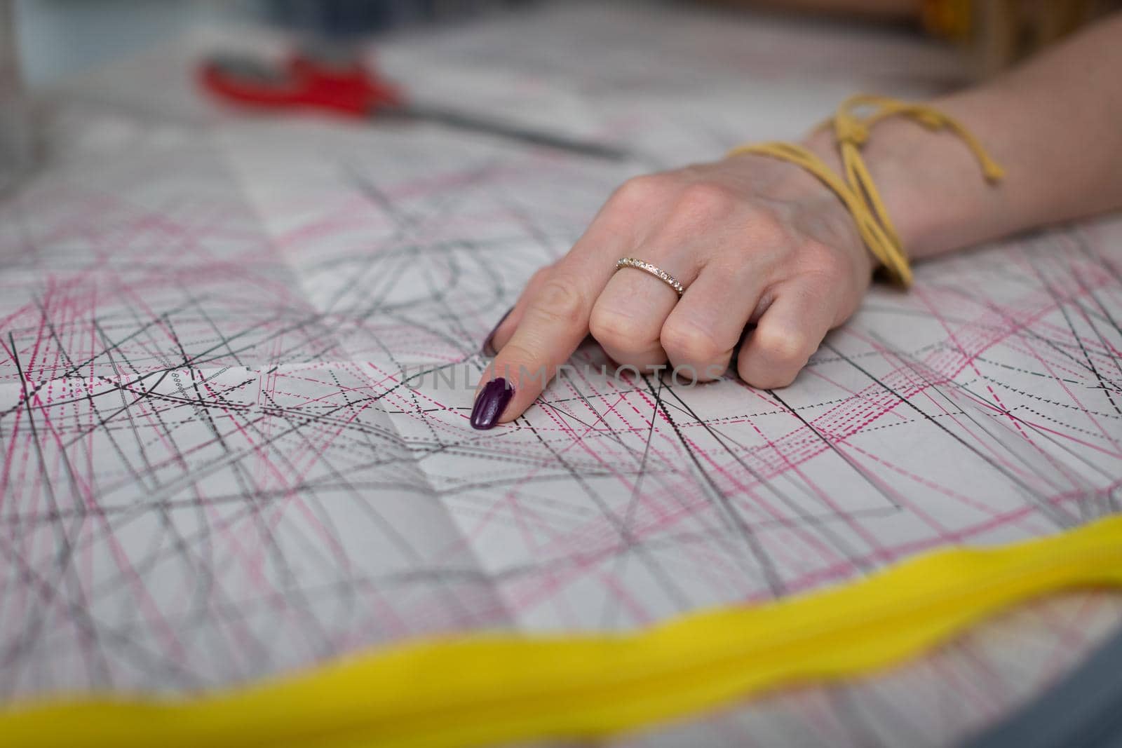 A woman's index finger shows lines in a sundry paper pattern. A tailor's workshop up close.