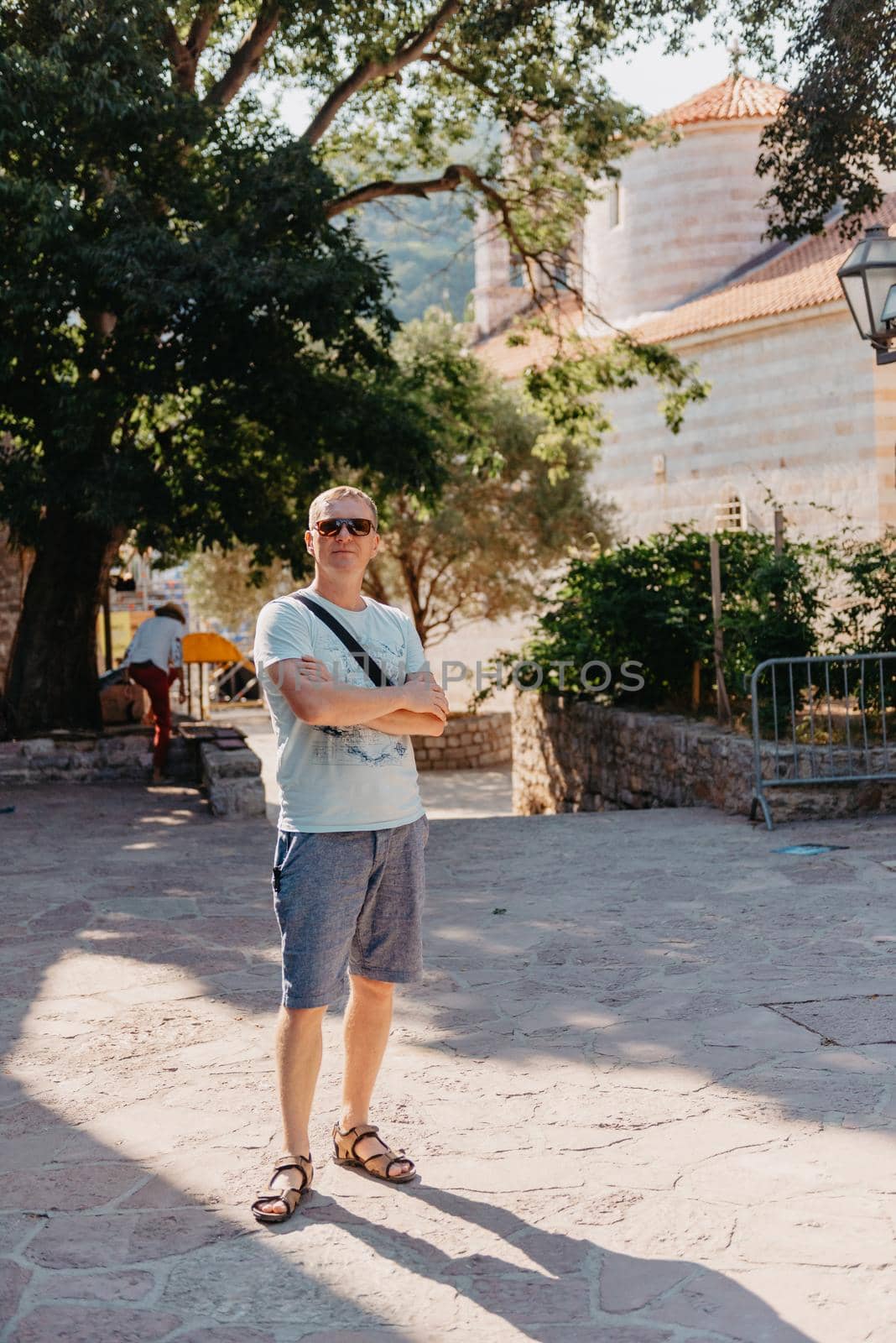 A handsome young man standing and smiling happily in the background of urban buildings. Forty years old caucasian tourist man outdoor near old city buildings - summer holiday.