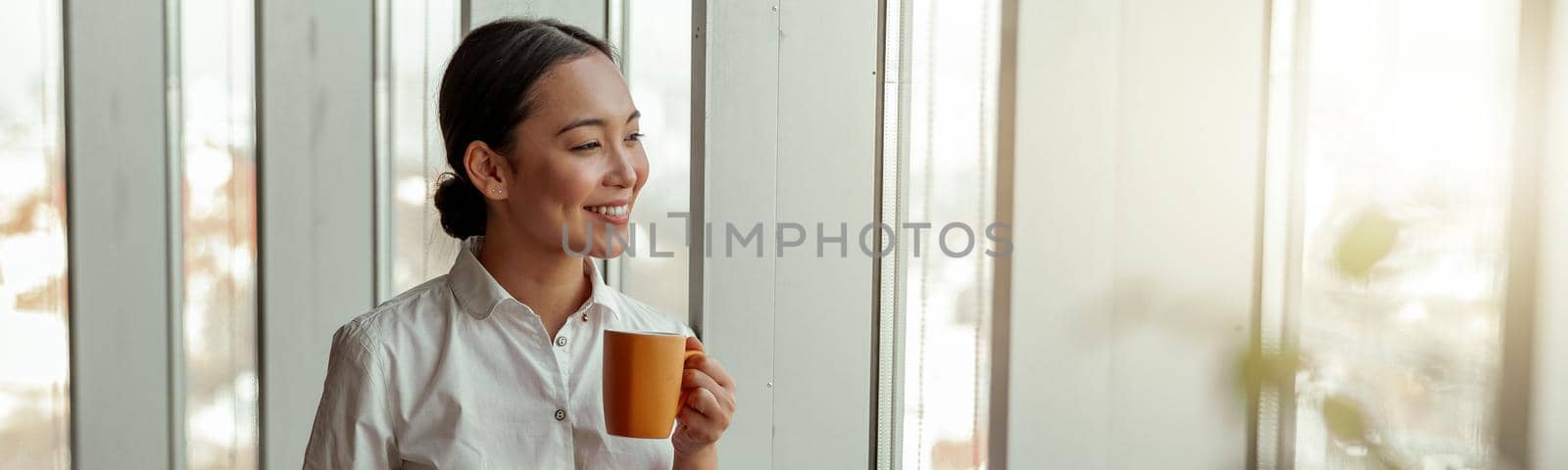 Portrait of asian business woman drinking coffee standing near windows at office. Blurred background