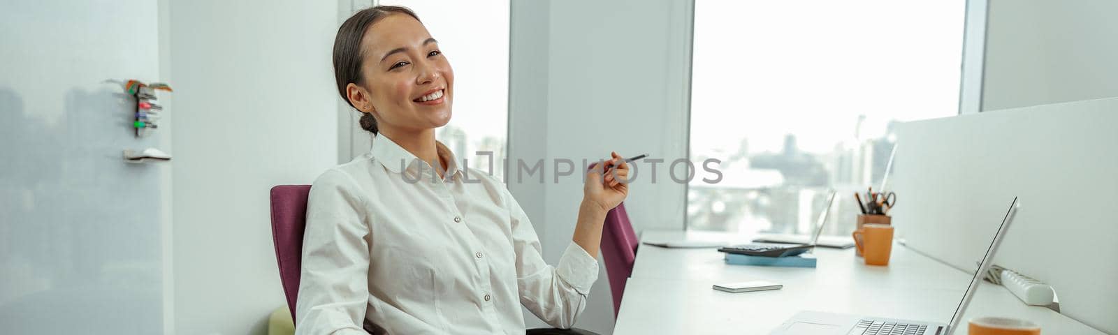 Smiling asian business woman sitting in office on her workplace and looks away. High quality photo