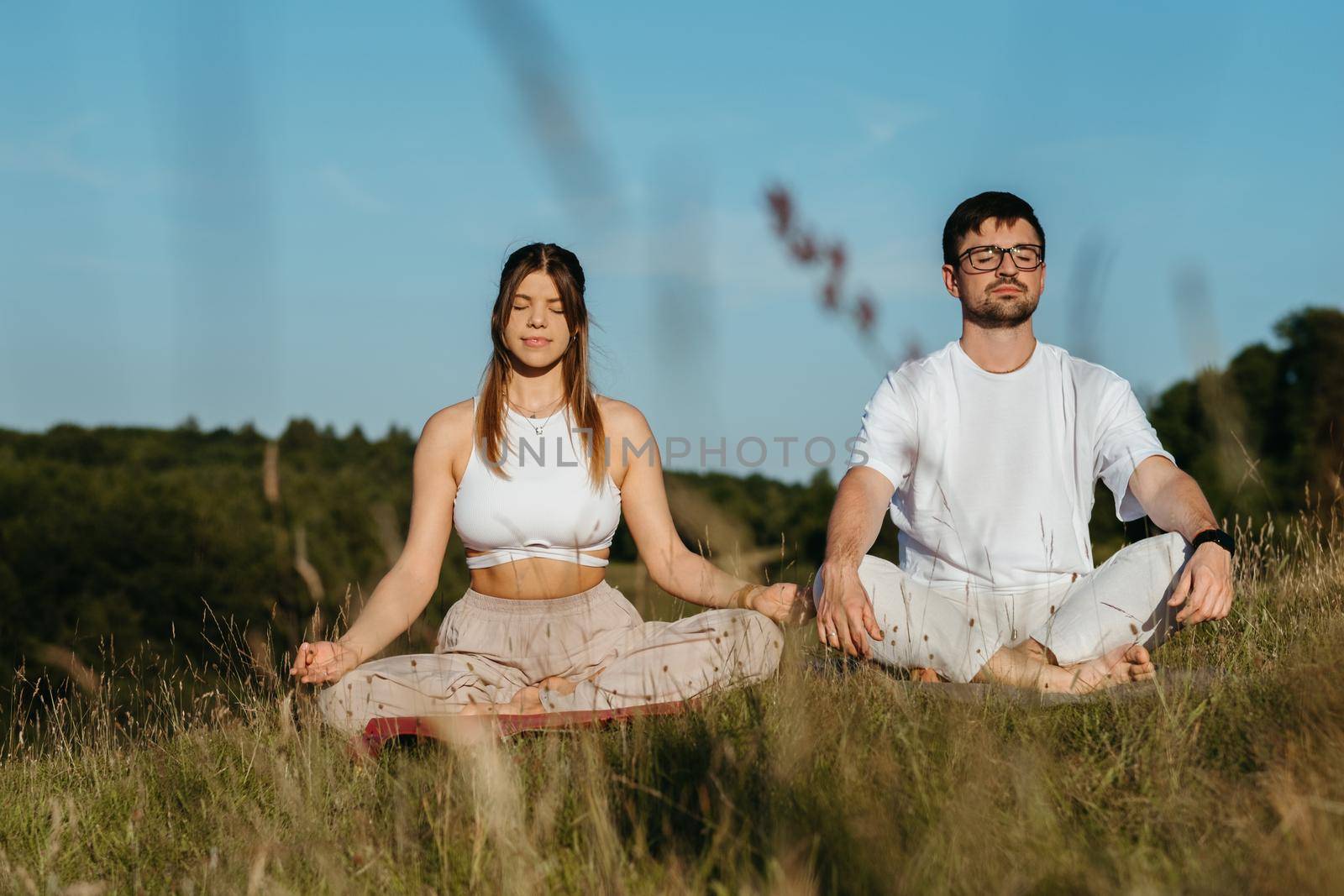 Young Adult Couple Meditating Outdoors, Caucasian Woman and Man Dressed Alike Breathing Fresh Air in the Nature by Romvy