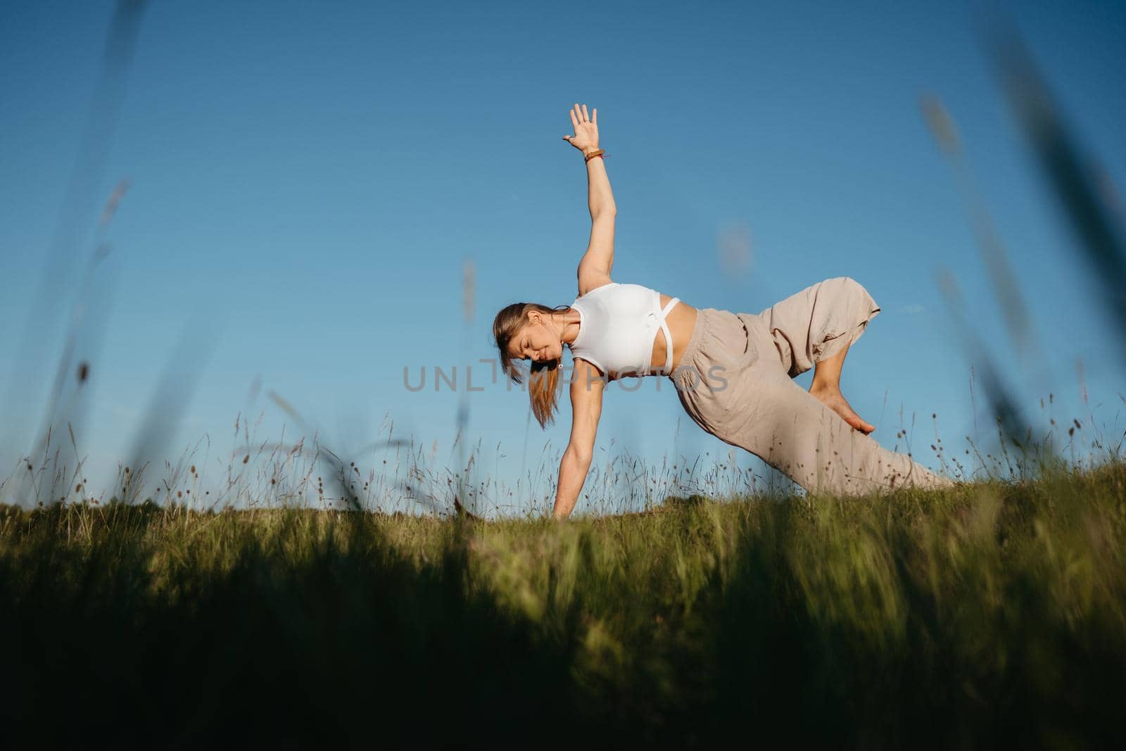 Young Woman Practicing Yoga Outdoors in the Field with Blue Sky on the Background by Romvy