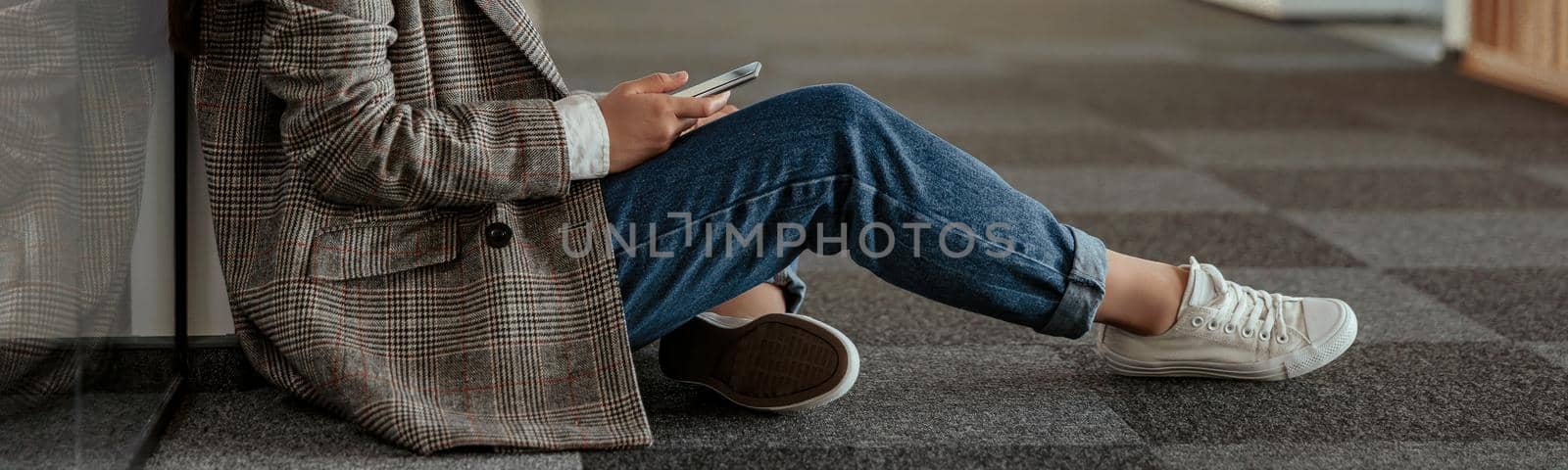 Happy asian business woman with phone sitting on floor in office and looks away by Yaroslav_astakhov